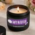 Candle in a black container with a purple label reading 'Empty Nester Echo' on a neutral background.